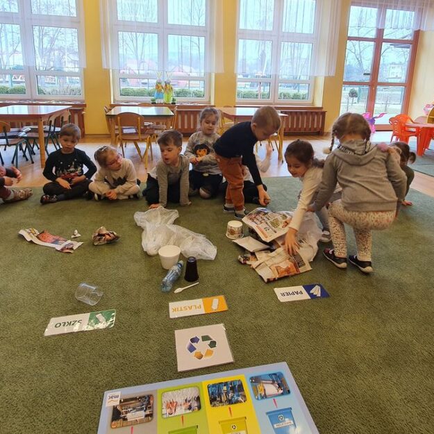 Grupka dzieci siedząca na dywanie poznaje różne rodzaje śmieci