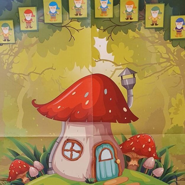 Na korkowej tablicy przypięty plakat przedstawiający dużego muchomora wokół którego są okienka z naklejonymi krasnalami. Plakat tworzy "Książkową Wioskę Krasnoludka"