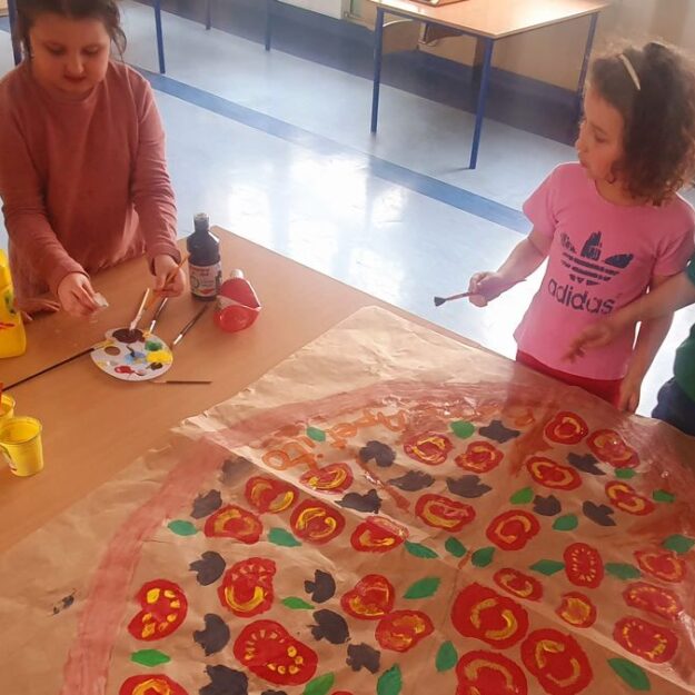 Uczniowie malują włoską pizzę na dużym arkuszu szarego papieru - praca zbiorowa