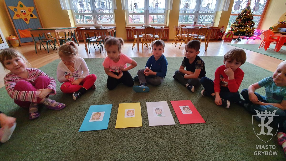 Dzieci siedzą na dywanie, przed nimi cztery karty z emocjami: smutek, radość, strach, złość