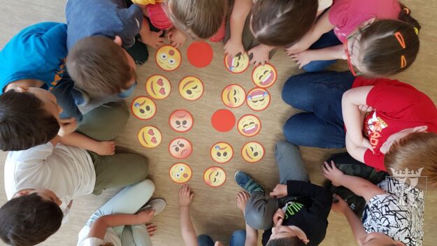 Dzieci siedzą na podłodze i grają w memory z emotikonami