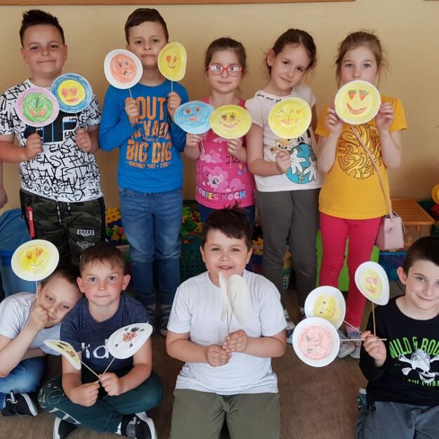 Grupa dzieci prezentująca swoje emotikony na patykach