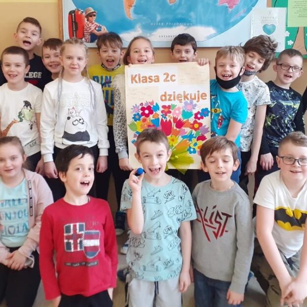 Grupa dzieci prezentująca duży plakat z napisem "Dziękujemy" oraz kwiatami