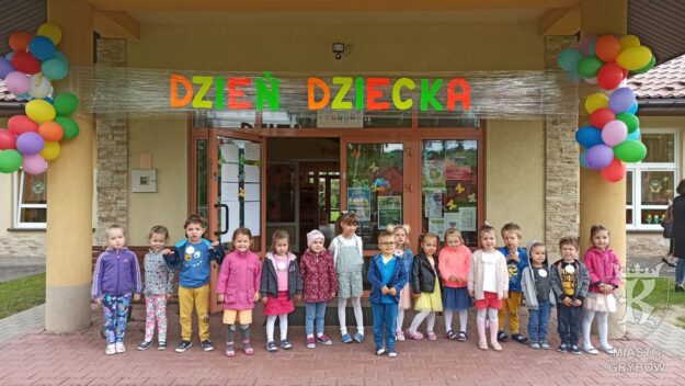 Zdjęcie grupowe dzieci przed placówką. Nad nimi wisi duży neonowy napis Dzień Dziecka