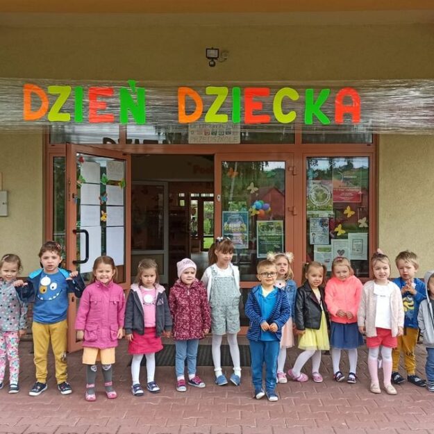 Zdjęcie grupowe dzieci przed placówką. Nad nimi wisi duży neonowy napis Dzień Dziecka