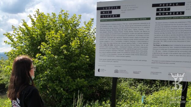 Uczennica odczytująca informacje dotyczące historii cmentarza żydowskiego oraz projektu "Ludzie, nie liczby"