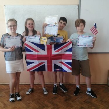 Uczniowie klasy 6c - Amelia, Julia, Sebastian i Szymon trzymają przed sobą rozłożoną flagę Wielkiej Brytanii oraz prezentują otrzymane dyplomy