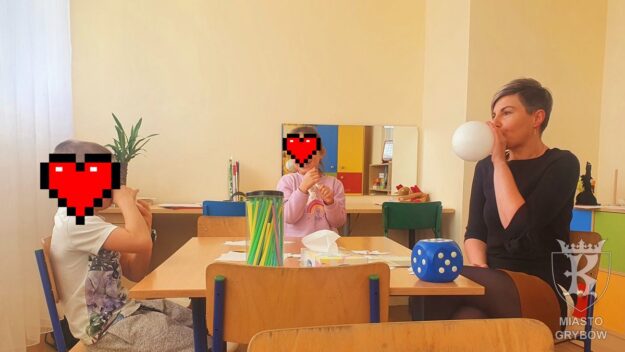 Zajęcia specjalistyczne prowadzone przez szkolnego logopedę - dzieci oraz logopeda siedząc przy stoliku nadmuchują balony