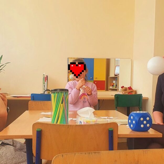 Zajęcia specjalistyczne prowadzone przez szkolnego logopedę - dzieci oraz logopeda siedząc przy stoliku nadmuchują balony