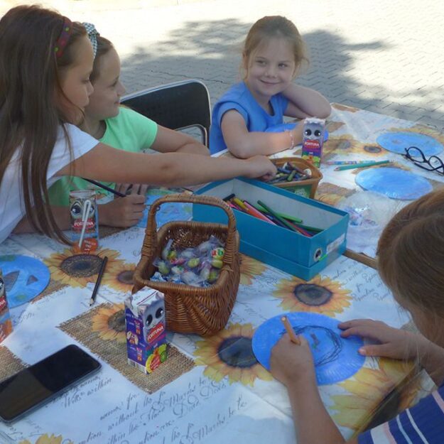 Uśmiechnięte dzieci siedzące przy stole w trakcie trwania zajęć plastycznych