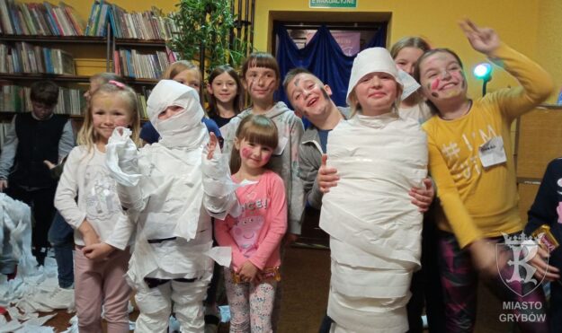 Uśmiechnięte dzieci owijają chłopca w papier toaletowy i tworzą mumię