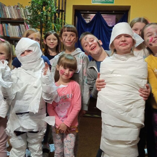 Uśmiechnięte dzieci owijają chłopca w papier toaletowy i tworzą mumię