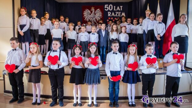 Dzieci ubrane na galowo stoją i trzymają w rękach serca