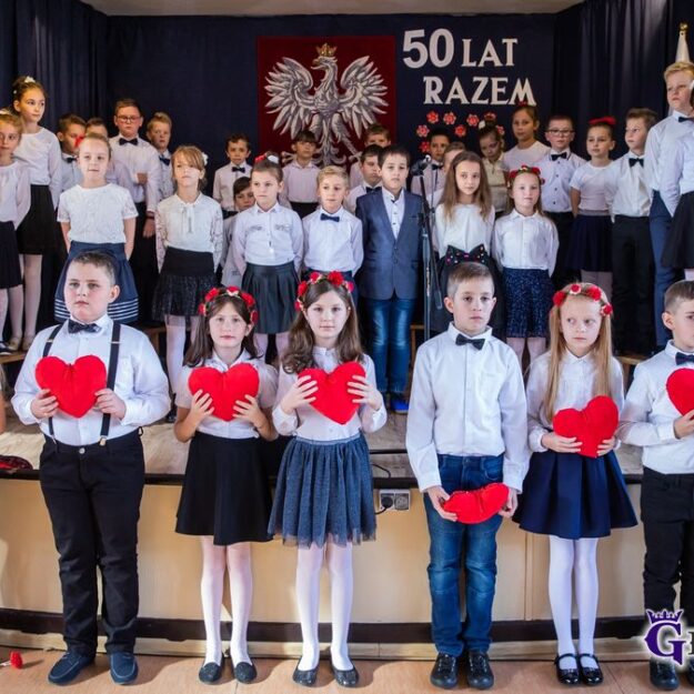 Dzieci ubrane na galowo stoją i trzymają w rękach serca