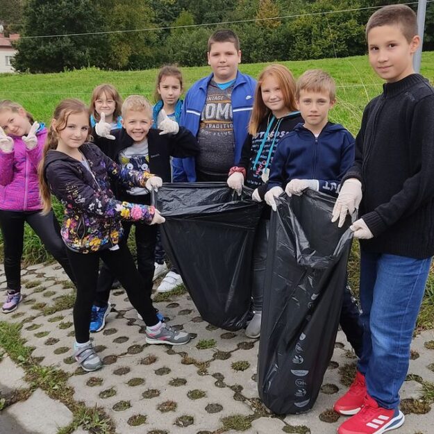 Uczniowie stojący na chodniku i prezentujący zebrane śmieci