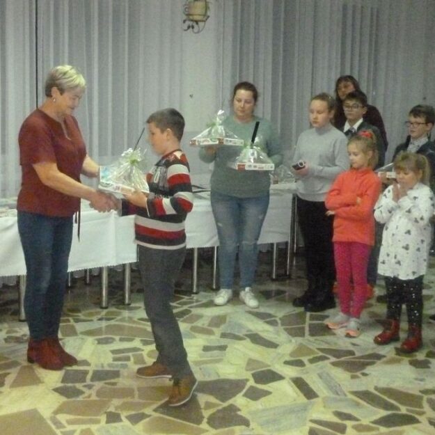 Pani gratuluje chłopcu trzymającemu nagrodę w tle dzieci