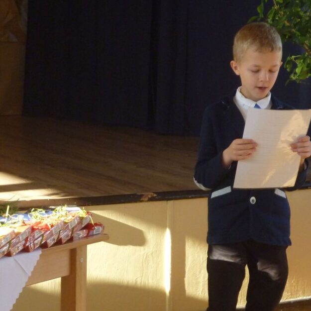 Chłopczyk stoi i czyta wiersz na stole obok nagrody