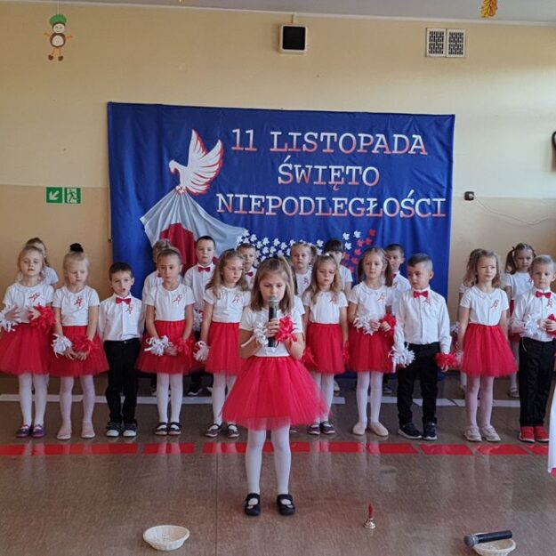 Dziewczynka śpiewa do mikrofonu, dwaj chłopcy machają flagami