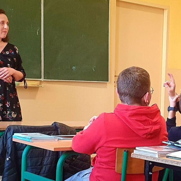 Widok na salę z uczniami, w tle przy tablicy pani prowadząca zajęcia