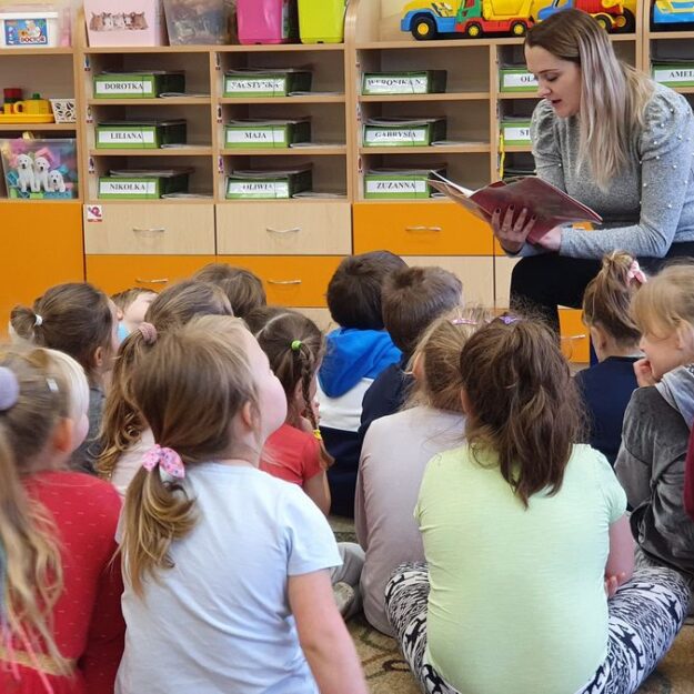 Pani czyta bajkę grupie dzieci, które siedzą na dywanie