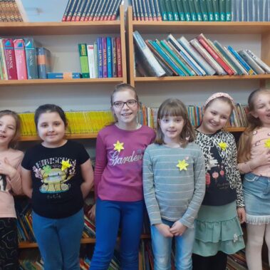 Grupa dzieci w bibliotece, w tle regały z książkami