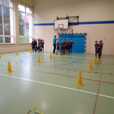 Dzieci stoją w trzech rzędach przed torem treningowym, obok nich trener