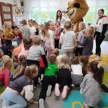 Dzieci otaczają lwa, obok stoją wychowawcy