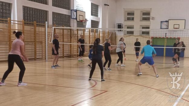 Grupa ludzi na sali gimnastycznej gra w siatkówkę