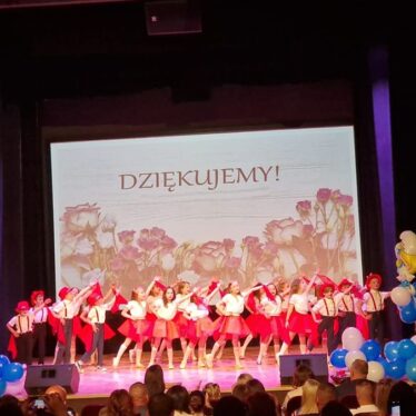 Dzieci tańczą do piosenki, trzymają dłoń uniesioną do góry