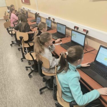 Grupa dzieci siedzi przy laptopach i projektuje banknoty