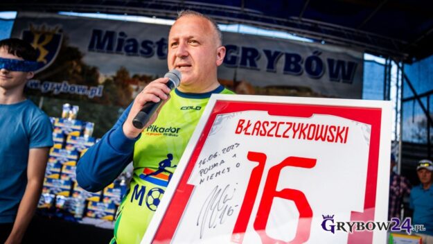 Mówiący do mikrofonu burmistrz prezentuje jedną z nagród - reprezentacyjną koszulkę podpisana przez Jakuba Błaszczykowskiego