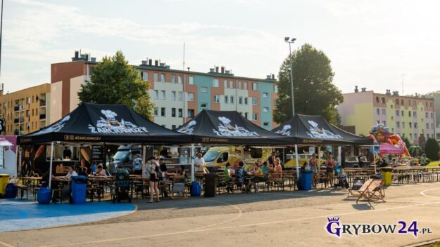 Widok na stoły, przy których siedzą klienci spożywające jedzenie przygotowane przez stojące obok foodtrucki