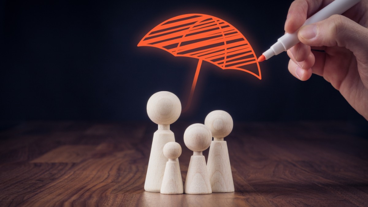 Postacie symbolizujące rodzinę a nad nimi narysowany pisakiem parasol symbolizujący ochronę. Z prawej dłoń trzymająca pisak