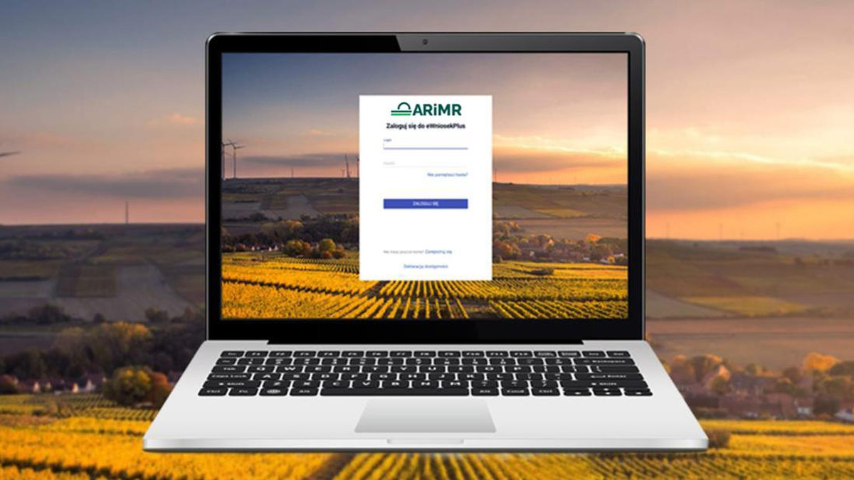 Otwarty laptop, w tle widok na pola i lasy