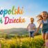 Uśmiechnięte dzieci biegną po łące w słońcu, obok kolorowego napisu „Małopolski Dzień Dziecka”