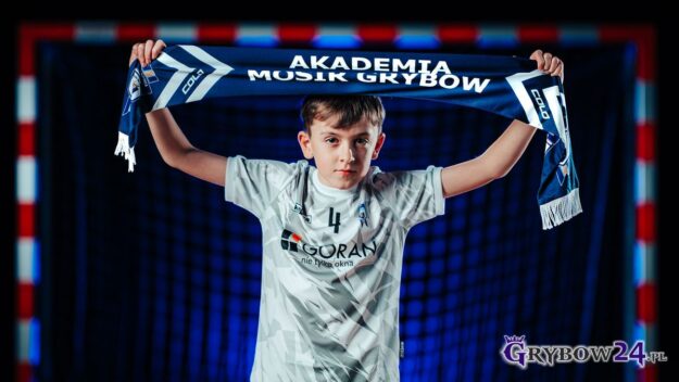 Sportowa przygoda czeka! Akademia MOSiR Grybów zaprasza Młody zawodnik Akademii MOSiR Grybów trzyma nad głową klubowy szalik na tle bramki sportowej