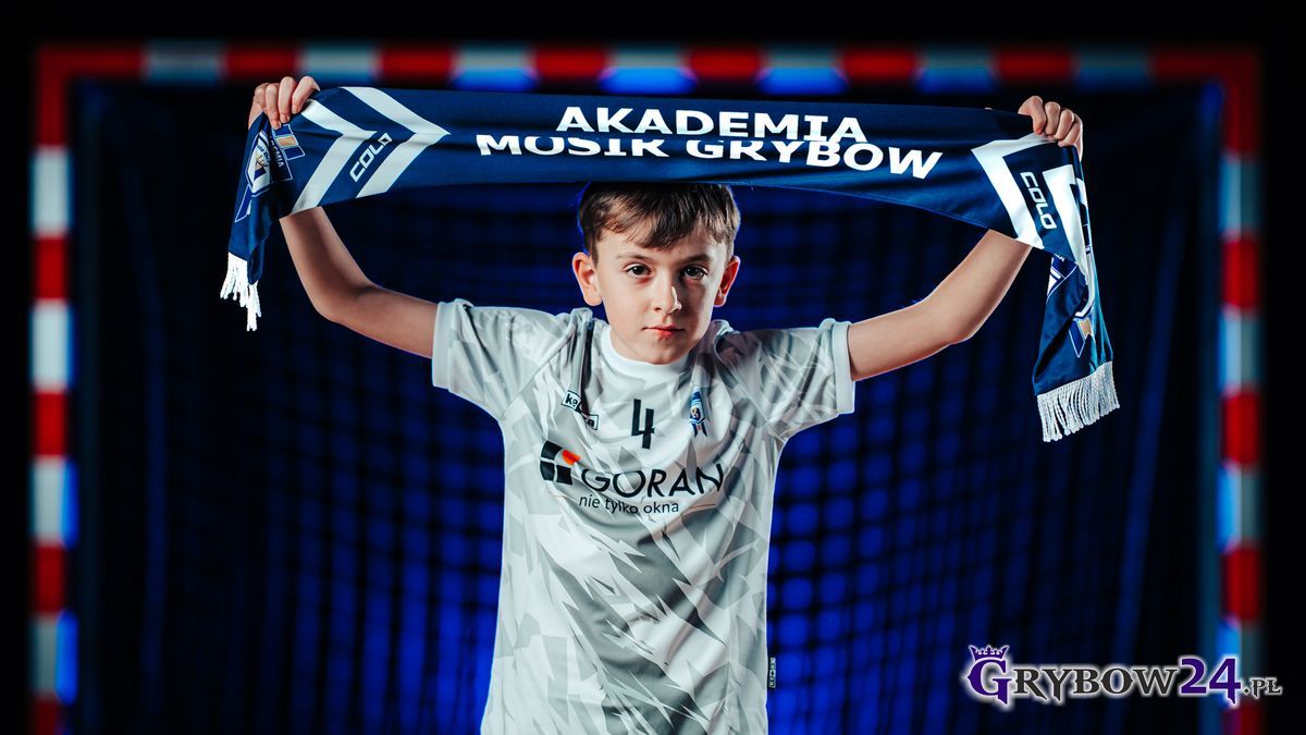 Sportowa przygoda czeka! Akademia MOSiR Grybów zaprasza Młody zawodnik Akademii MOSiR Grybów trzyma nad głową klubowy szalik na tle bramki sportowej
